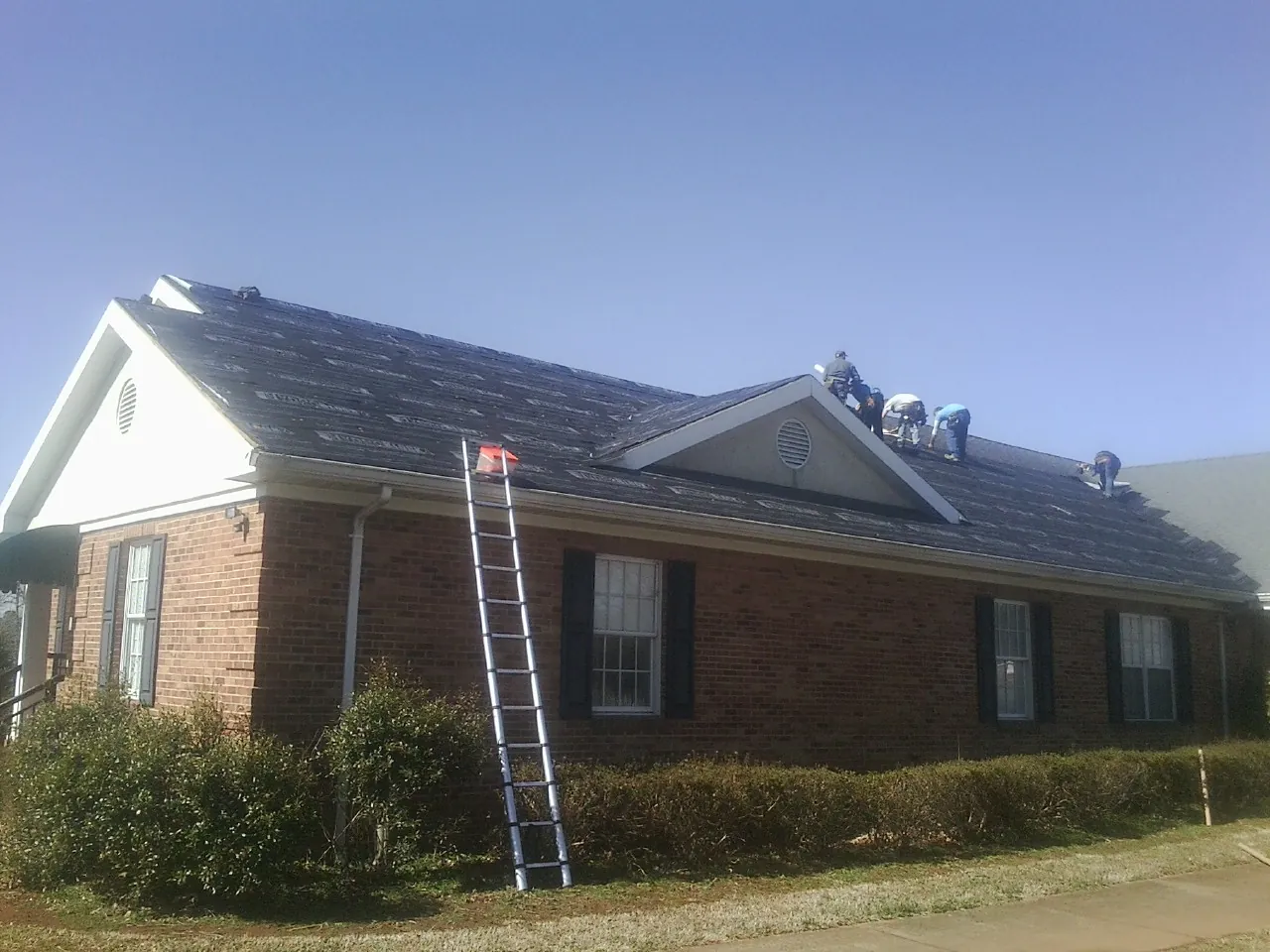 Crew tearing shingles off a brick ranch roof with a ladder set — Metal Roof Repair work by our crew in Deep Run