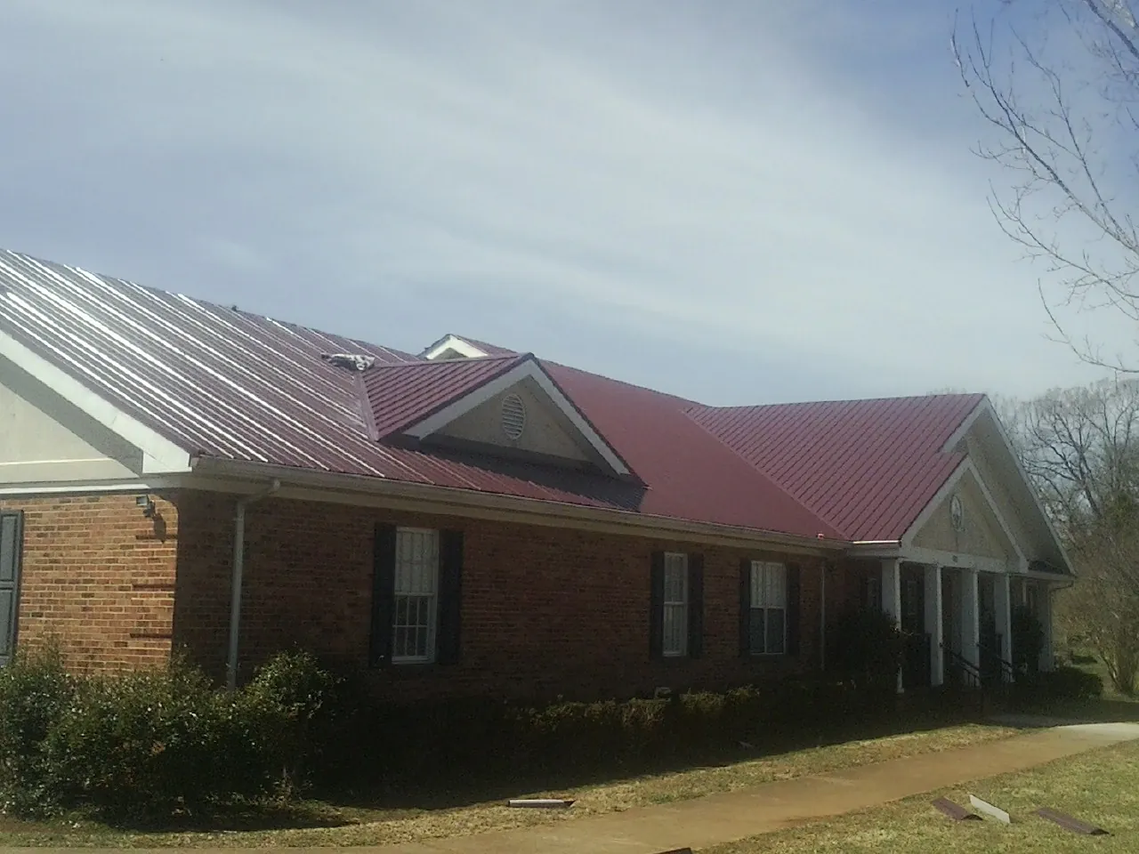 Red metal roof with gabled entries on a long brick building, from a Hail Damage Roof Repair job in Deep Run