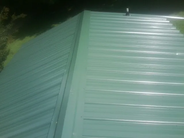New green metal panels meeting at the ridge of a roof — Flat Roof Repair work by our crew in Deep Run