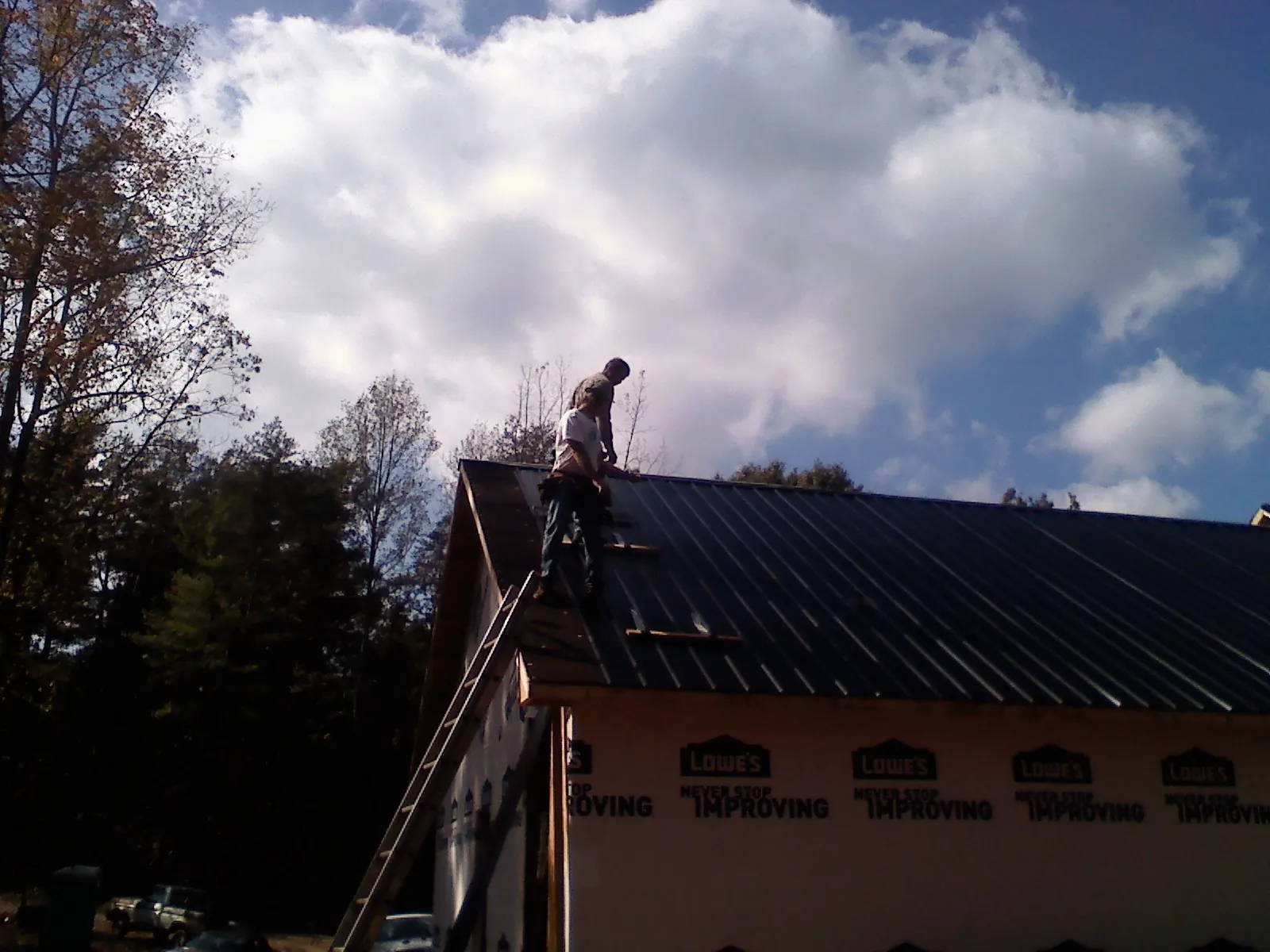 Roofer fastening dark metal panels high against a cloudy sky, from a Roof Inspection job in Deep Run