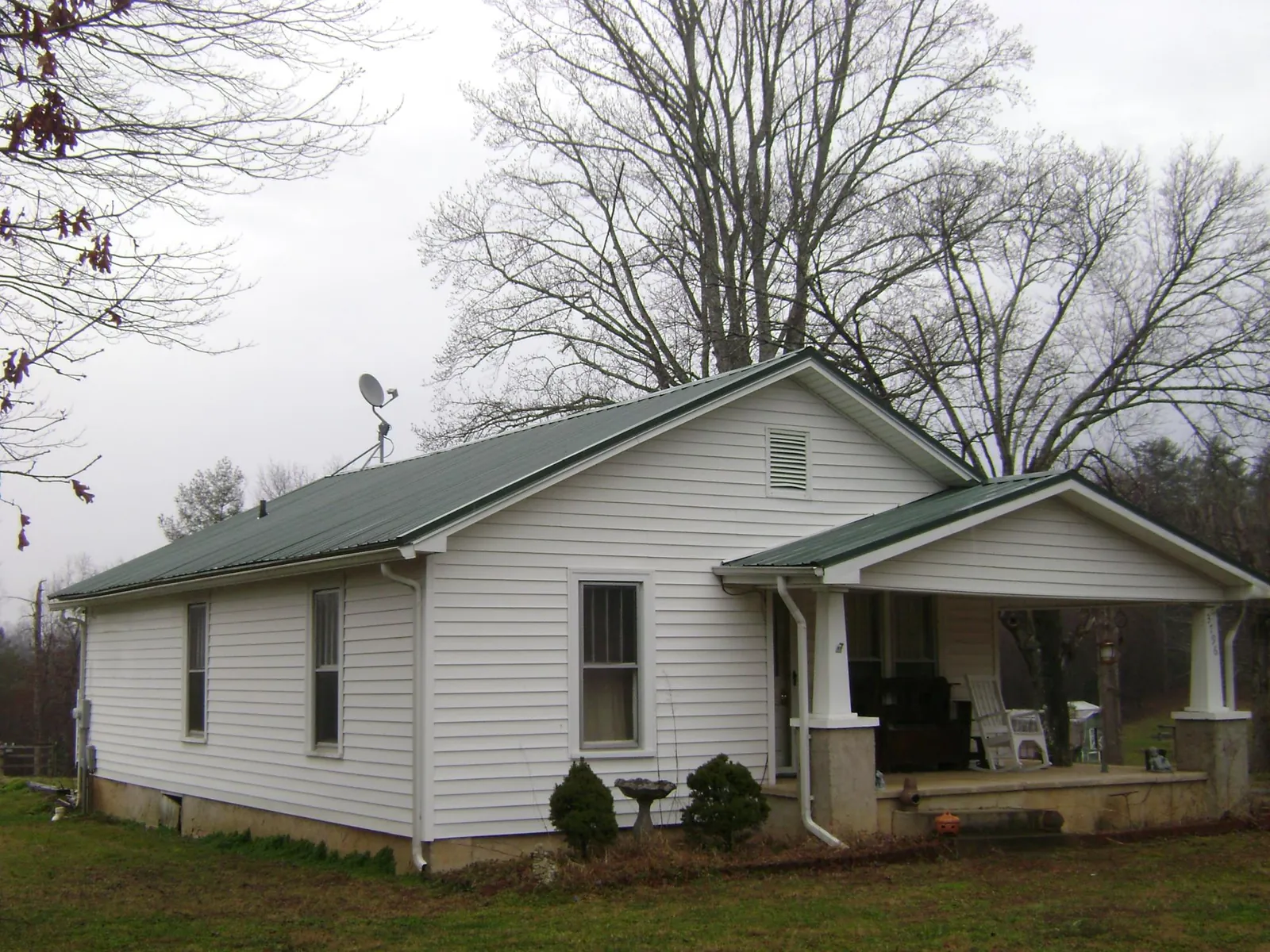 Green metal roof on a white bungalow with a side porch in Deep Run